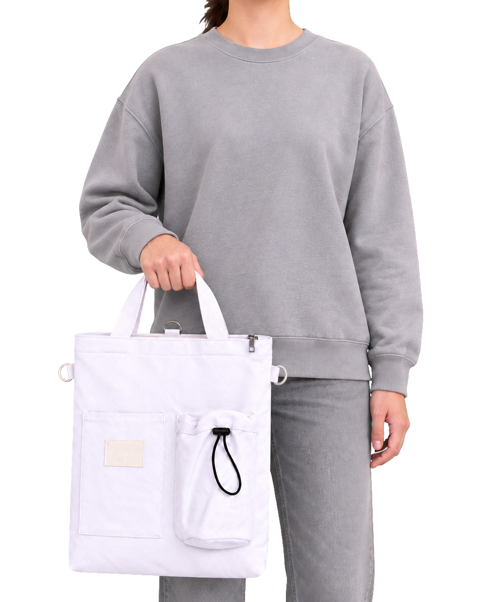 The white canvas tote carried in one hand by its two short top handles, a small pale woven label on the front pocket